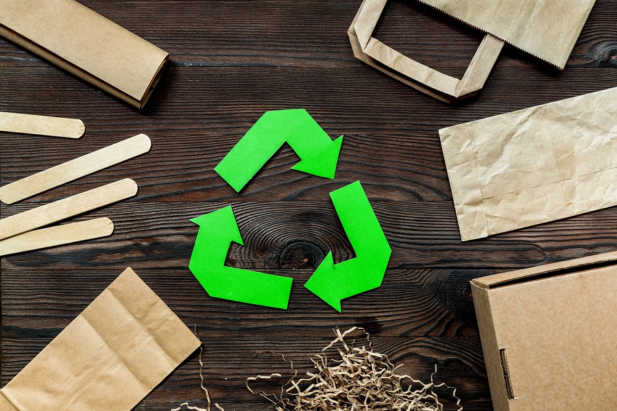 Paper recycle sign with paper and carton garbage on wooden background top view.